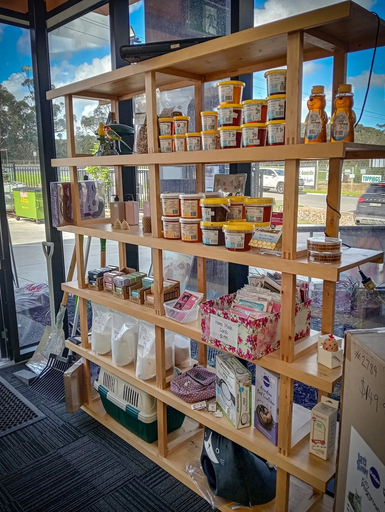 Timber display shelves with local honey, jams and specialty goods near large window, with parrot perched on top